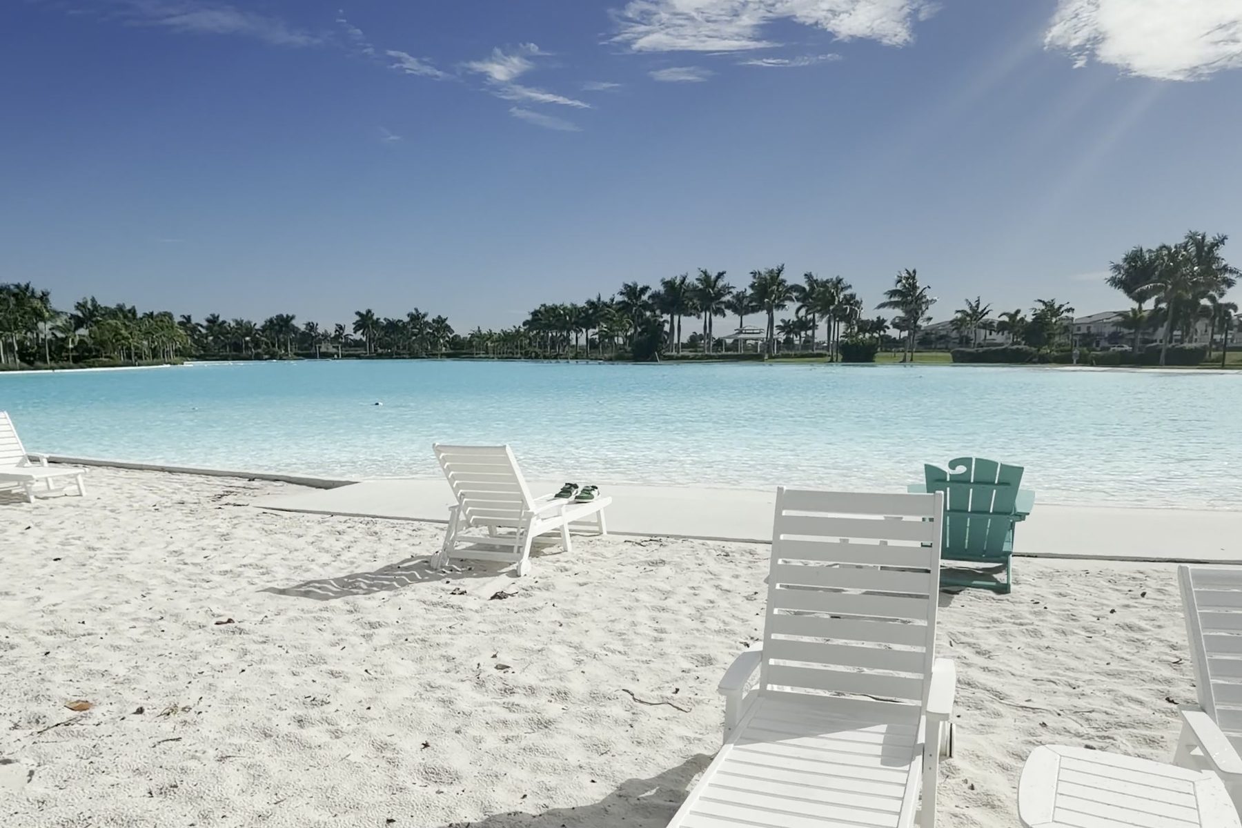 The lagoon at Aqua in Bradenton: white sand, white lounge chairs, clear blue water and a line of palm trees.
