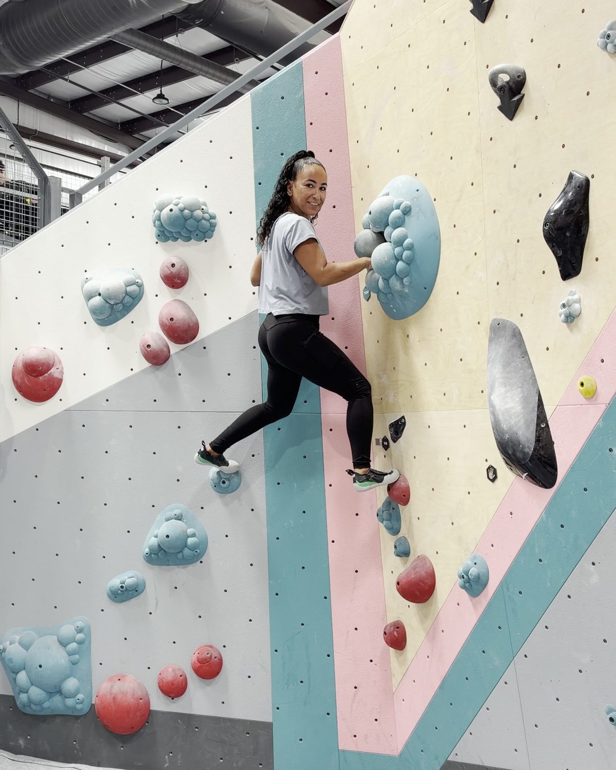 Sekina climbing across a pink and teal bouldering wall.